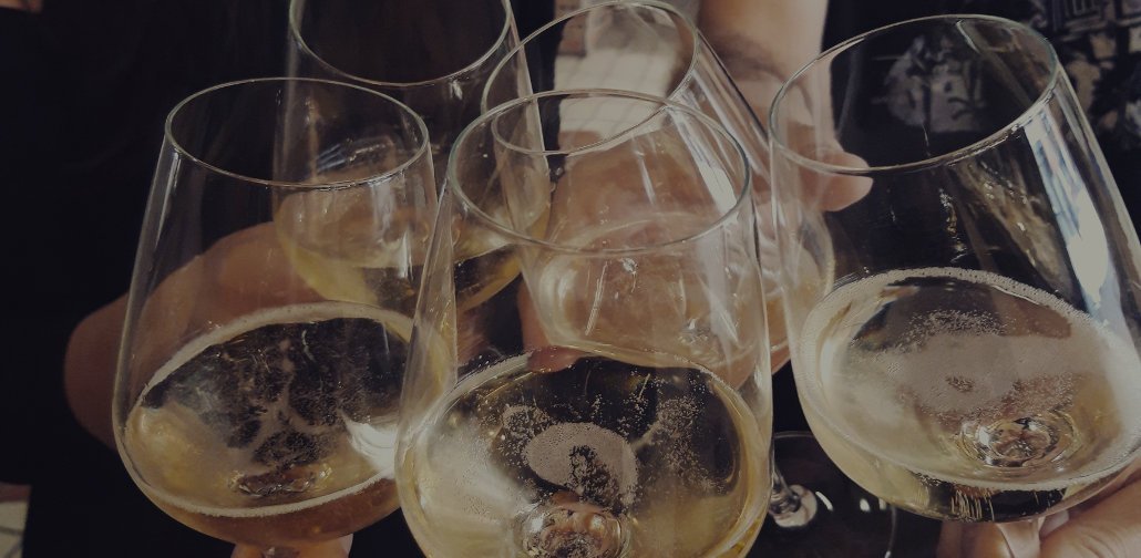 Close-up of several people clinking glasses of sparkling white wine in a celebratory toast. The glasses are held together, and bubbles are visible in the drinks.