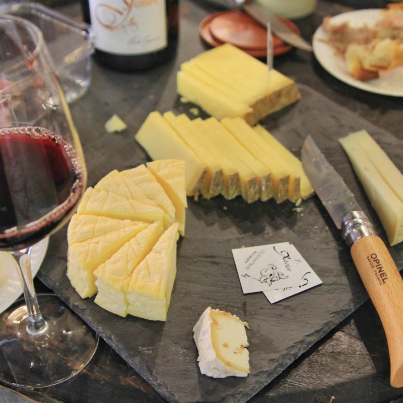 Un plateau d'ardoise avec un assortiment de fromages en tranches, un couteau à fromage, un verre de vin rouge et une assiette avec du pain évoquent les saveurs du Marché Victor Hugo-parfaites après une visite guidée. Un petit morceau de fromage et une étiquette sont posés sur le plateau. Un plateau d'ardoise avec un assortiment de fromages en tranches, un couteau à fromage, un verre de vin rouge et une assiette avec du pain évoquent les saveurs du Marché Victor Hugo-parfaites après une visite guidée. Un petit morceau de fromage et une étiquette sont posés sur le plateau.