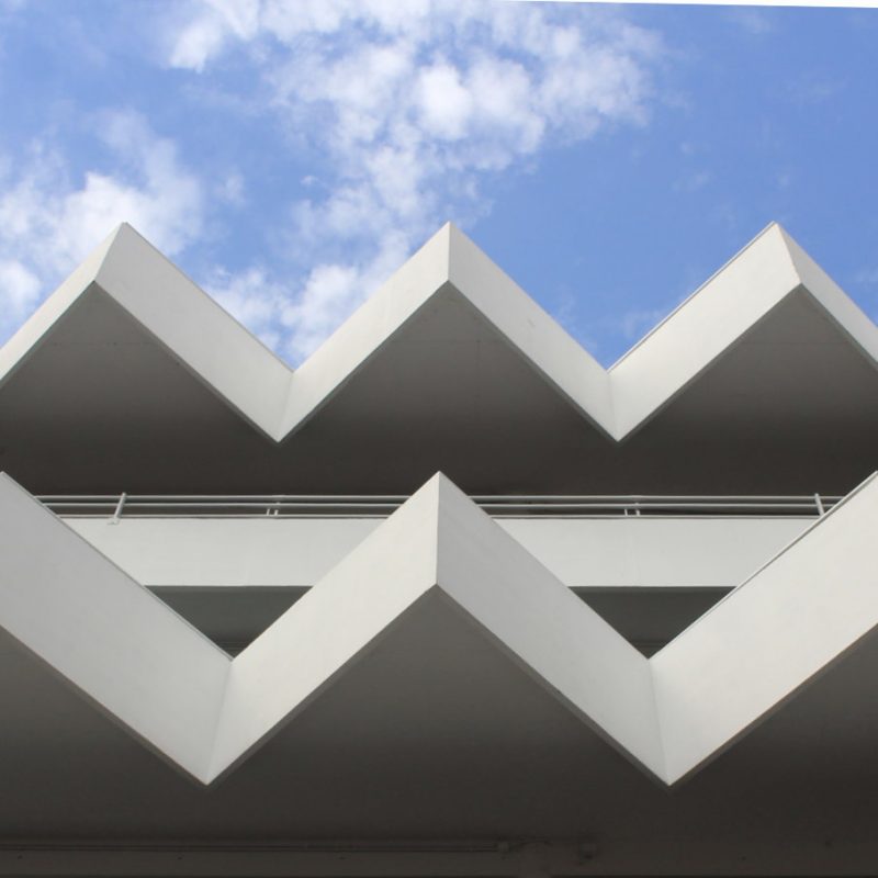 A modern building with a striking zigzag roof design, viewed from below against a blue sky with scattered clouds—its sharp geometric lines echo the bold architectural style of Victor Hugo Market.