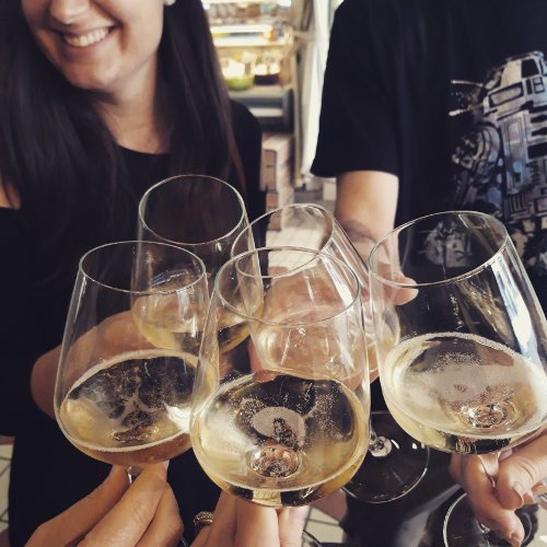 Quatre personnes trinquent en buvant des verres de vin blanc, peut-être après une visite guidée au Marché Victor Hugo, avec deux personnes partiellement visibles et une femme souriante à l'arrière-plan. Quatre personnes trinquent en buvant des verres de vin blanc, peut-être après une visite guidée au Marché Victor Hugo, avec deux personnes partiellement visibles et une femme souriante à l'arrière-plan.