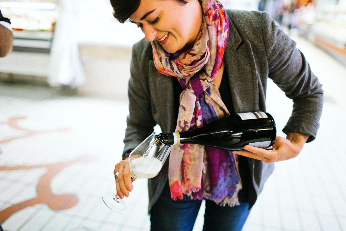 Une femme vêtue d'un foulard coloré et d'un blazer gris sourit en versant du vin dans un verre, à l'intérieur, sur un sol carrelé. Elle incarne l'esprit chaleureux de Toulouse et son amour du bon vin et du fromage. Une femme vêtue d'un foulard coloré et d'un blazer gris sourit en versant du vin dans un verre, à l'intérieur, sur un sol carrelé. Elle incarne l'esprit chaleureux de Toulouse et son amour du bon vin et du fromage.