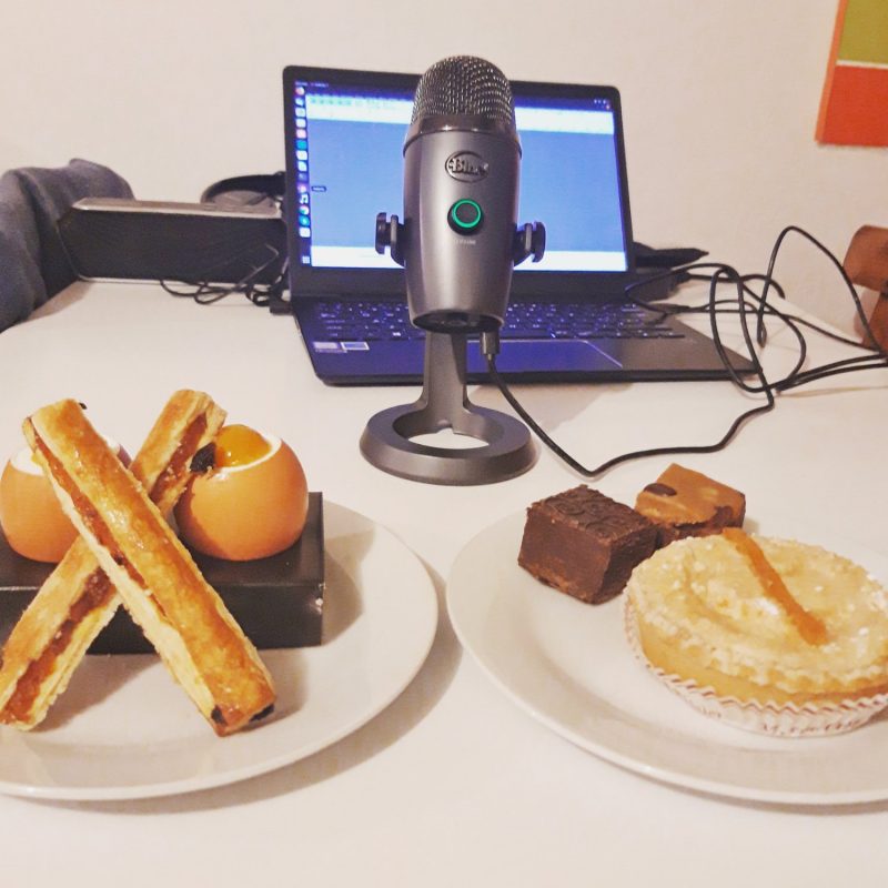 A table with two plates of assorted desserts sits in front of a microphone and an open laptop with audio software, hinting at a Podcast—perhaps for English Speakers of Toulouse sharing their Chocolate & Pastry Tour experiences.
