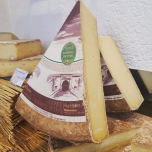 A close-up of several wedges of Comté Marcel Petite cheese, showing the label and aged rind, stacked together on a counter against a white textured wall—a perfect highlight for Taste of Toulouse Virtual Tasting Experiences. A close-up of several wedges of Comté Marcel Petite cheese, showing the label and aged rind, stacked together on a counter against a white textured wall—a perfect highlight for Taste of Toulouse Virtual Tasting Experiences.