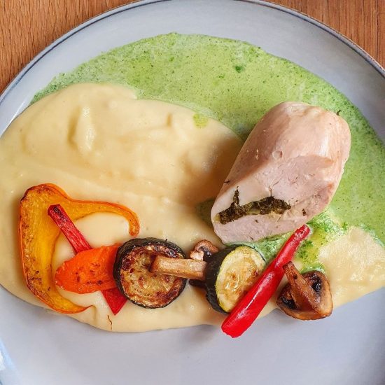 A plated dish inspired by Toulouse, featuring chicken breast stuffed with herbs, creamy mashed potatoes, green sauce, and sautéed vegetables—perfect for anyone seeking foodie things to do in the city.