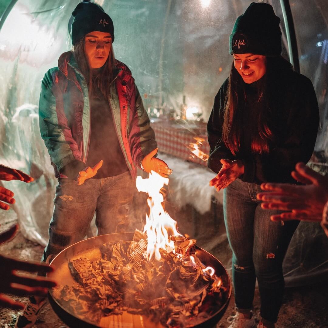 2 women cosying up next to La Friche Gourmande bon fire