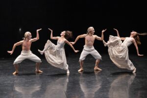 Four ballet dancers in pale, flowing costumes and white wigs perform synchronized, expressive poses on a dark stage—an elegant scene among the many things to do for arts enthusiasts visiting Toulouse’s vibrant tourist attractions.