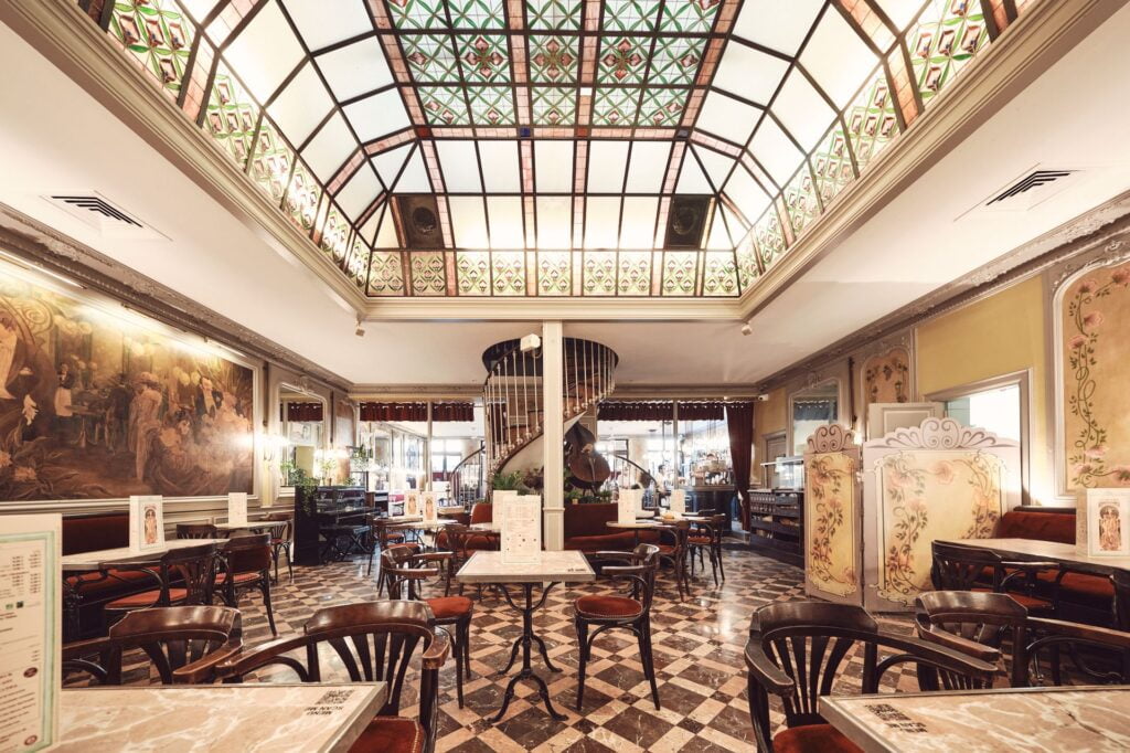 Elegant, vintage-style café with marble tables and a colorful stained-glass ceiling—perfect for those seeking a cozy, inviting spot to eat in Toulouse. Enjoy patterned tile floors, large murals, and the serene ambiance found in the best Toulouse restaurants.