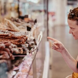 A woman points at a selection of cured meats displayed behind a glass counter during the Albi Gourmet Food Tour in a market or delicatessen.
