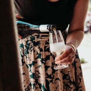 A person wearing a black top and floral skirt pours sparkling wine into a glass, its bubbles rising—a perfect toast to an unforgettable Albi Gourmet Food Tour.