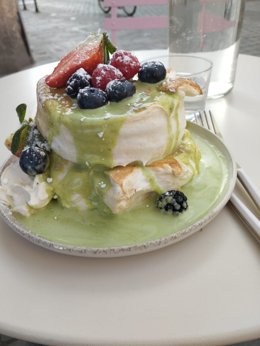 A stack of fluffy pancakes topped with strawberries, blueberries, and raspberries, drizzled with green matcha sauce and powdered sugar, sits on a plate—perfect for those seeking the best brunches in Toulouse.