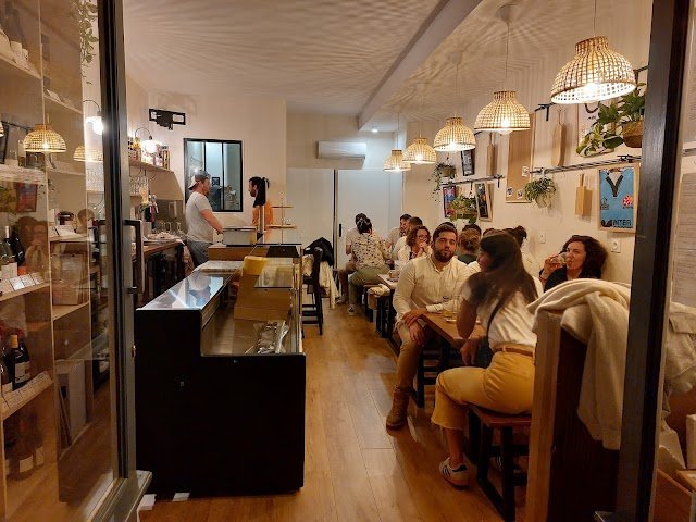 Chez Bobonne wine bar. A cozy, warmly lit restaurant in Toulouse with wooden floors and hanging wicker lamps. Diners sit closely at tables along the walls, chatting and enjoying their meals like in local wine bars while a chef works behind the counter.